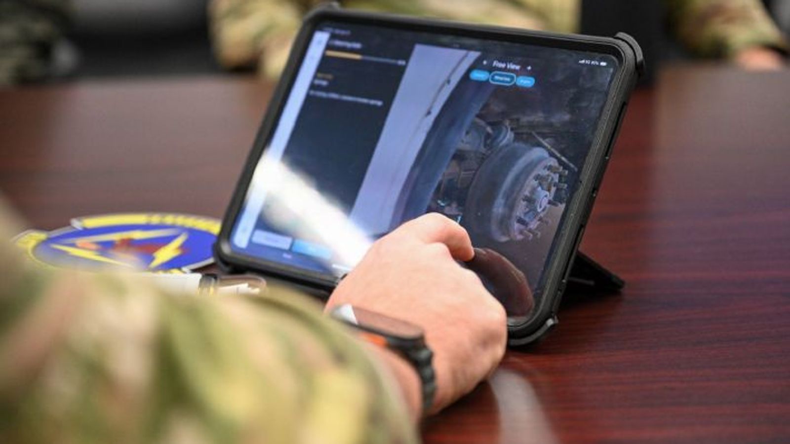 person in a military uniform shot from arm's length, interacting with the steering axle 3d model on a tablet