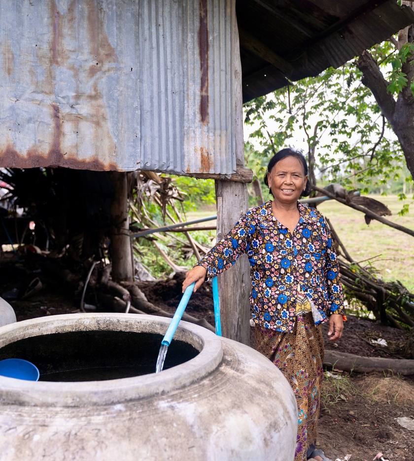 A woman drawing water from a covered well with a hose