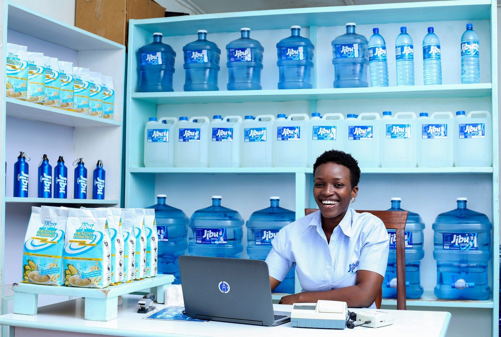 A woman working at a laptop in a shop stocked with bottled water