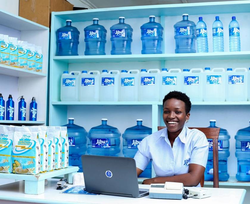 A woman working at a laptop in a shop stocked with bottled water