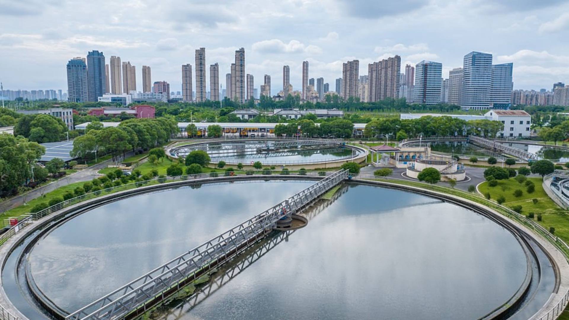 Aerial view of water treatment basins with a city skyline behind them.