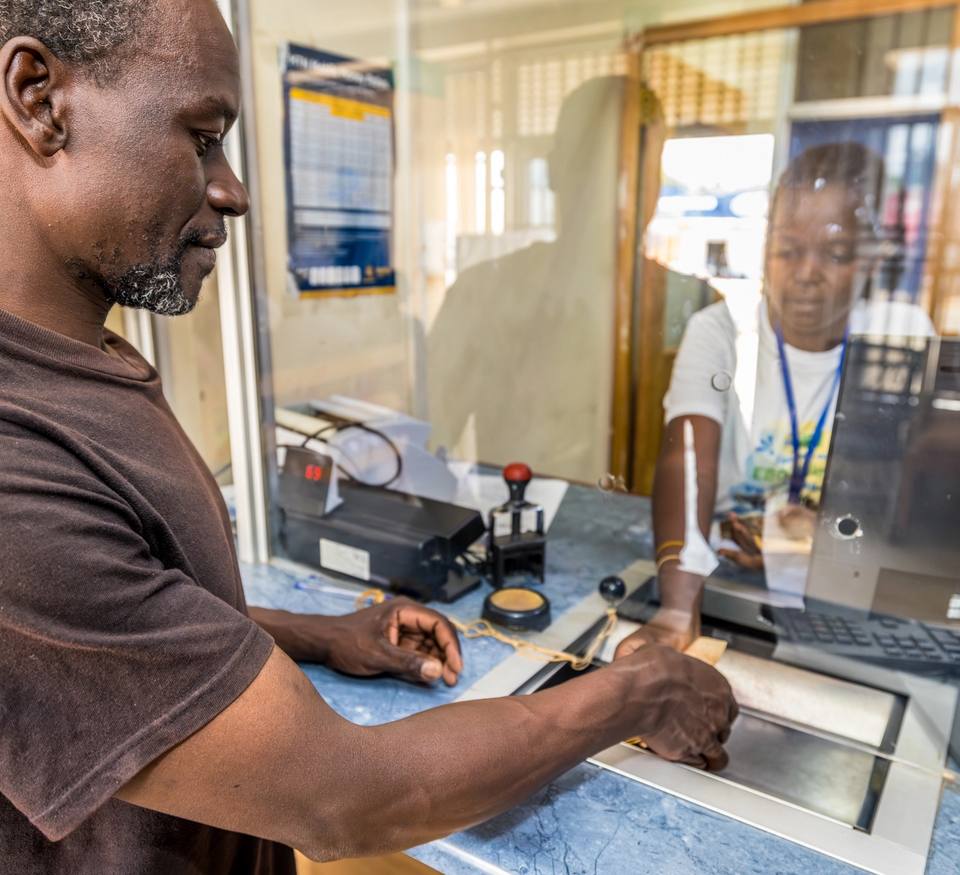 A man pays at the counter of a water enterprise while an employee helps him from behind the window.