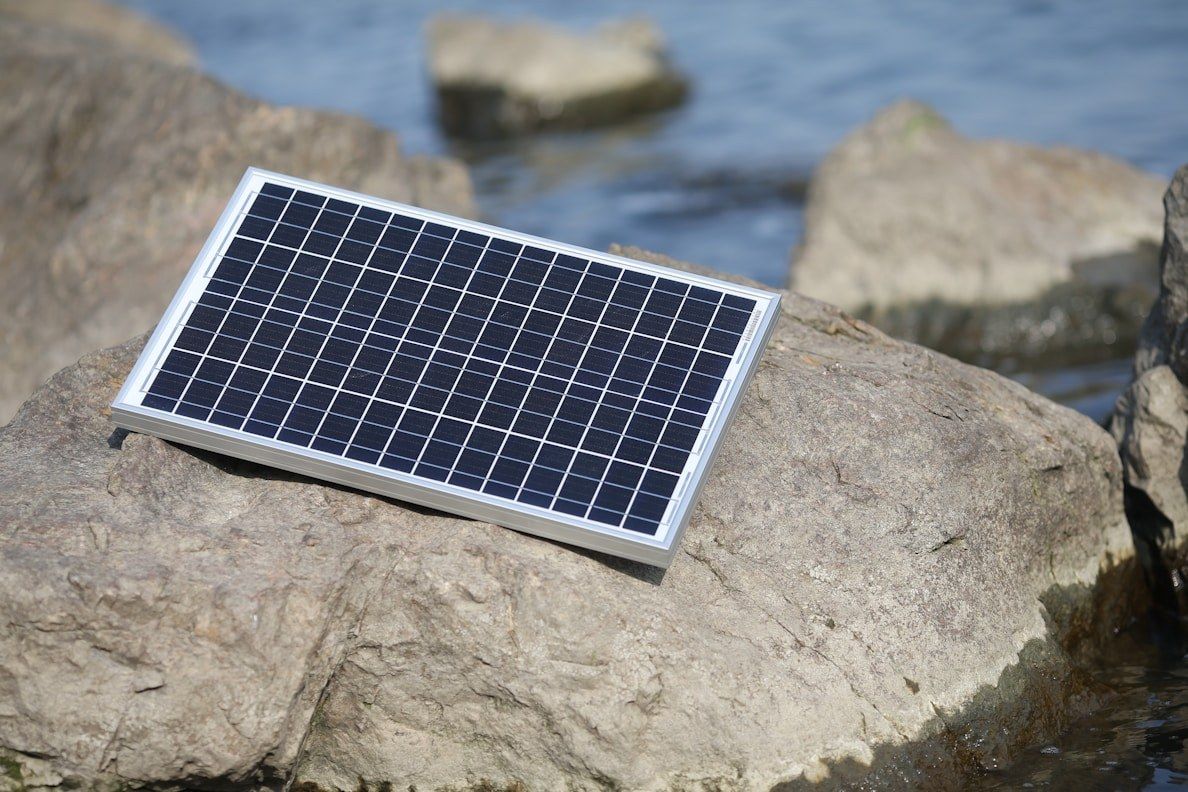 A small solar panel resting on rocks at the water's edge