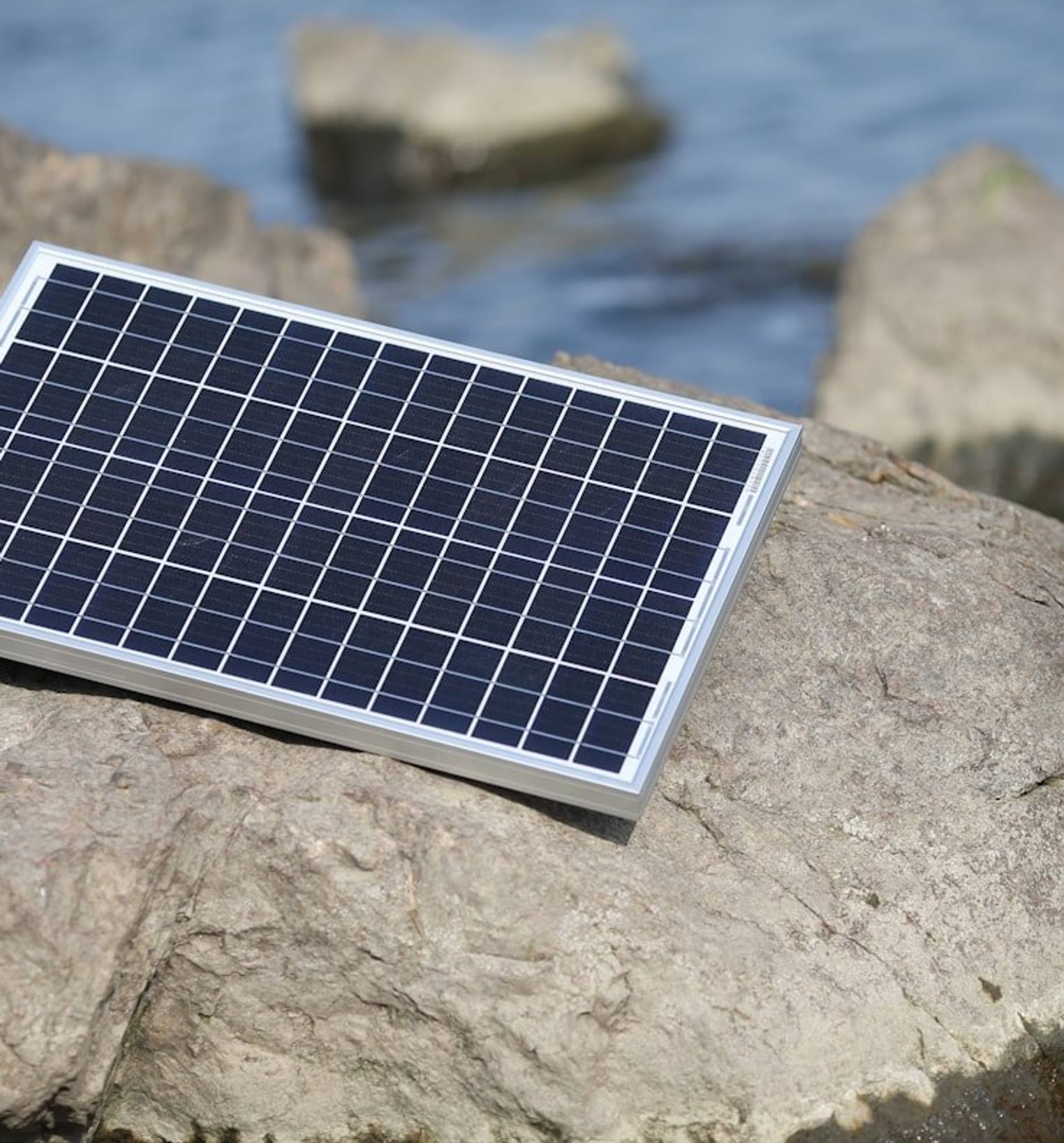 A small solar panel resting on rocks at the water's edge