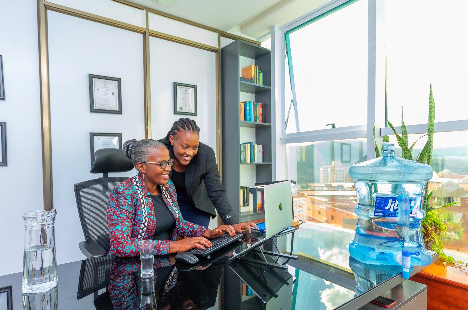 Two women looking at a laptop in an office beside a water cooler