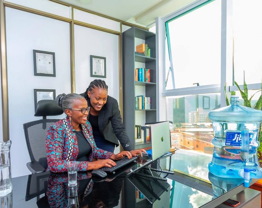 Two women looking at a laptop in an office beside a water cooler