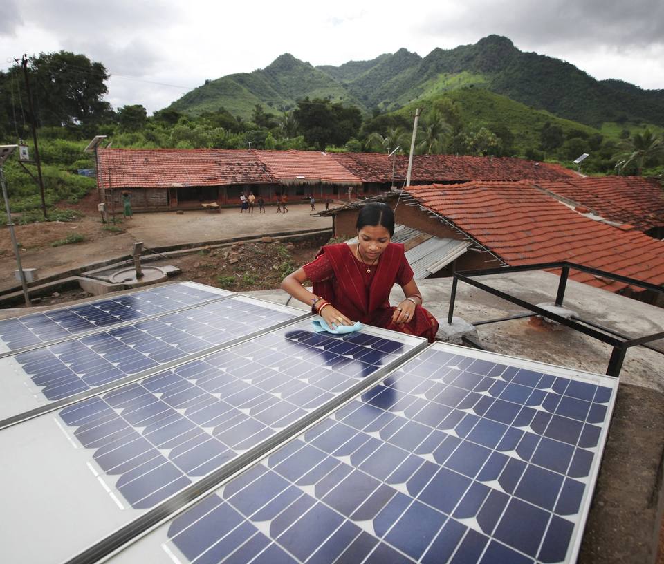 A woman cleans solar panels on a roof in rural India.