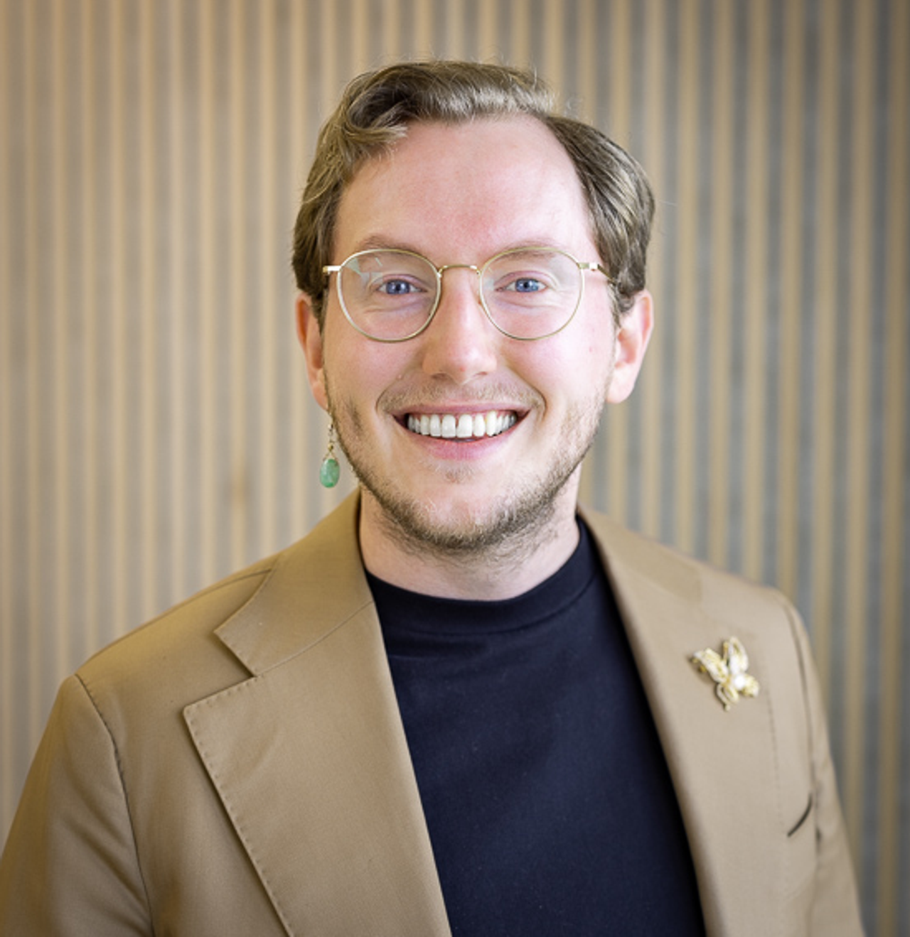 Portrait of Mr Sietse Blom in a beige jacket over a dark top, against a wooden slatted wall.