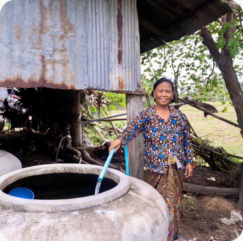 A woman drawing water from a covered rainwater tank beside her home