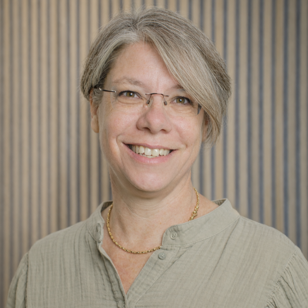Portrait of Ms Nicola Haigh in a sage green shirt, against a wooden slatted wall.