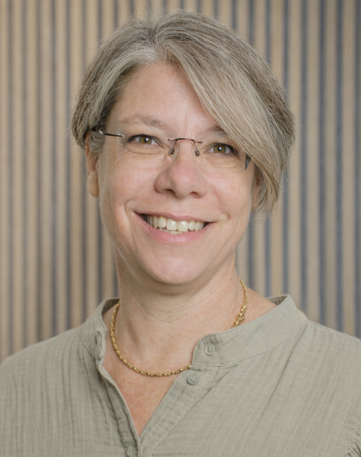 Portrait of Ms Nicola Haigh in a sage green shirt, against a wooden slatted wall.