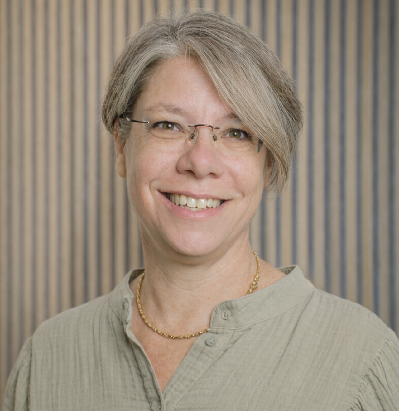Portrait of Ms Nicola Haigh in a sage green shirt, against a wooden slatted wall.