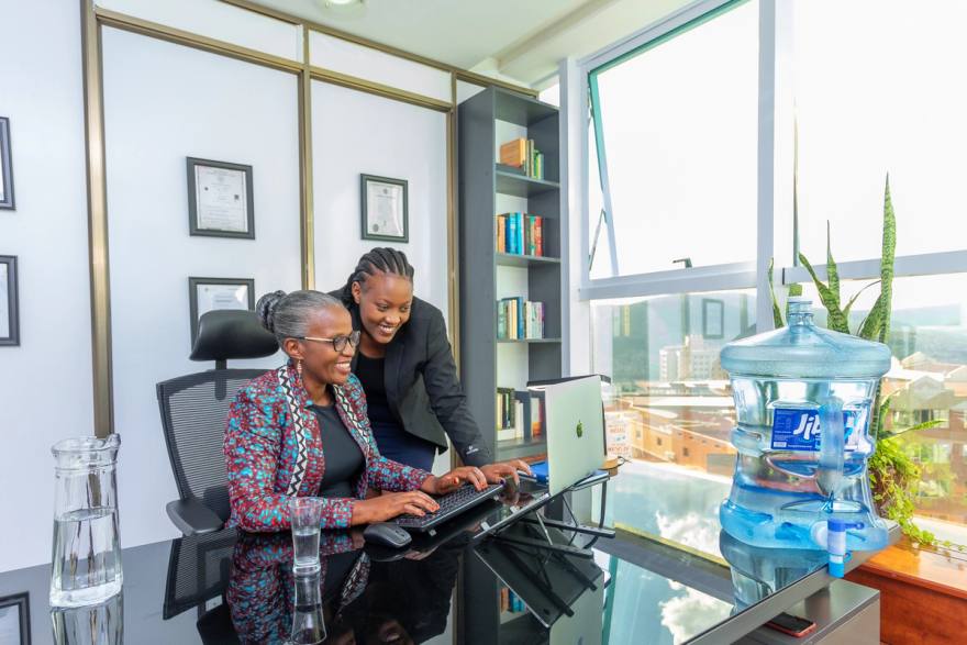 Twee vrouwen kijken samen naar een laptop aan een bureau in een kantoor, met een waterfles ernaast