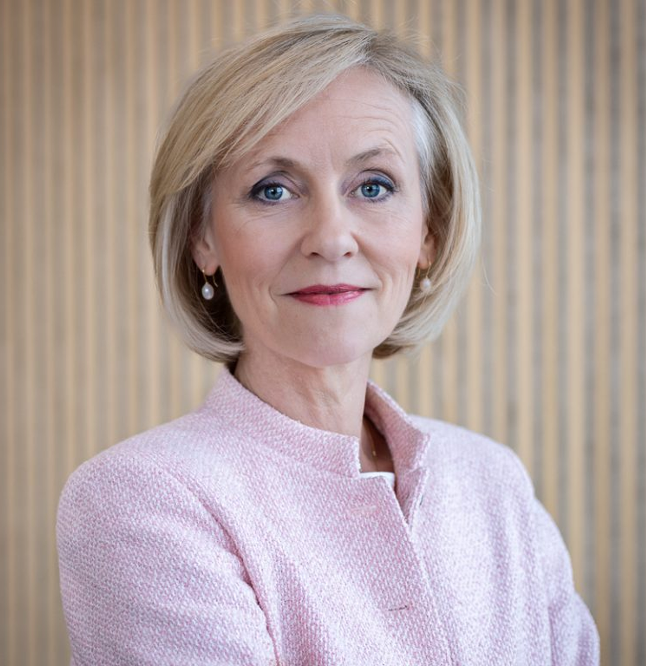 Portrait of Ms Josien Sluijs in a pale pink jacket, against a wooden slatted wall.