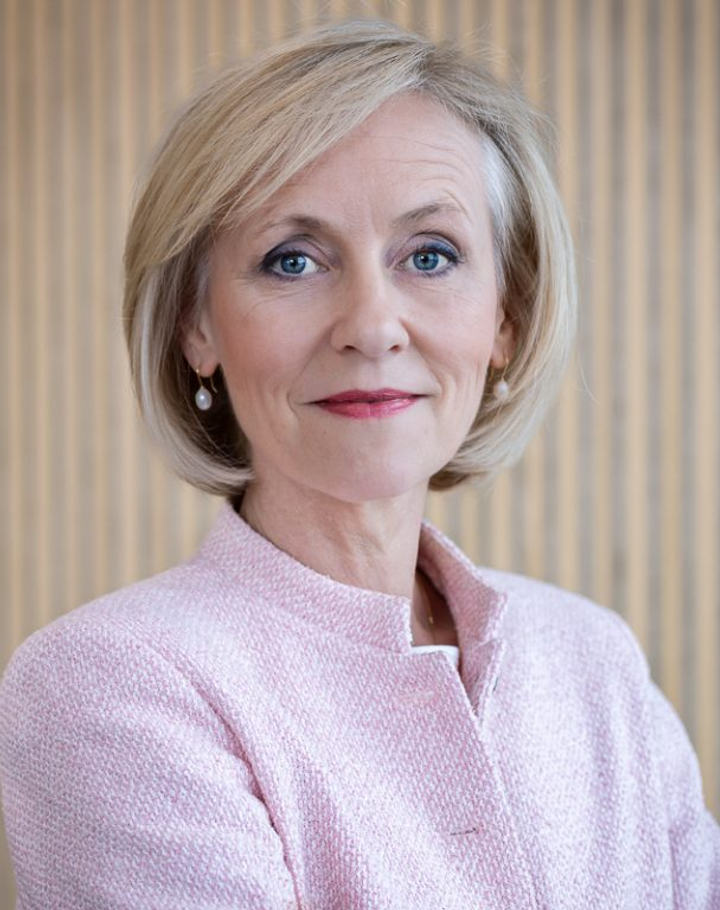 Portrait of Ms Josien Sluijs in a pale pink jacket, against a wooden slatted wall.