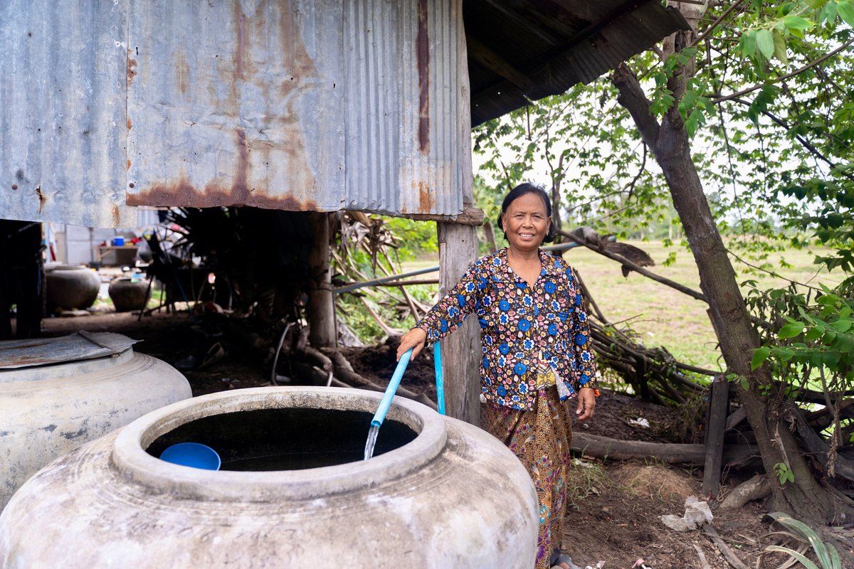 A woman standing beside a covered well with a hand pump
