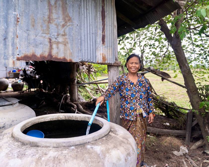 A woman standing beside a covered well with a hand pump