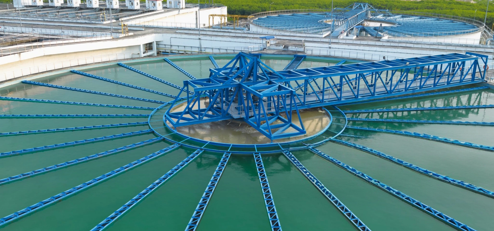 Blauwe ruimer boven een groen bezinkbassin van een waterzuivering