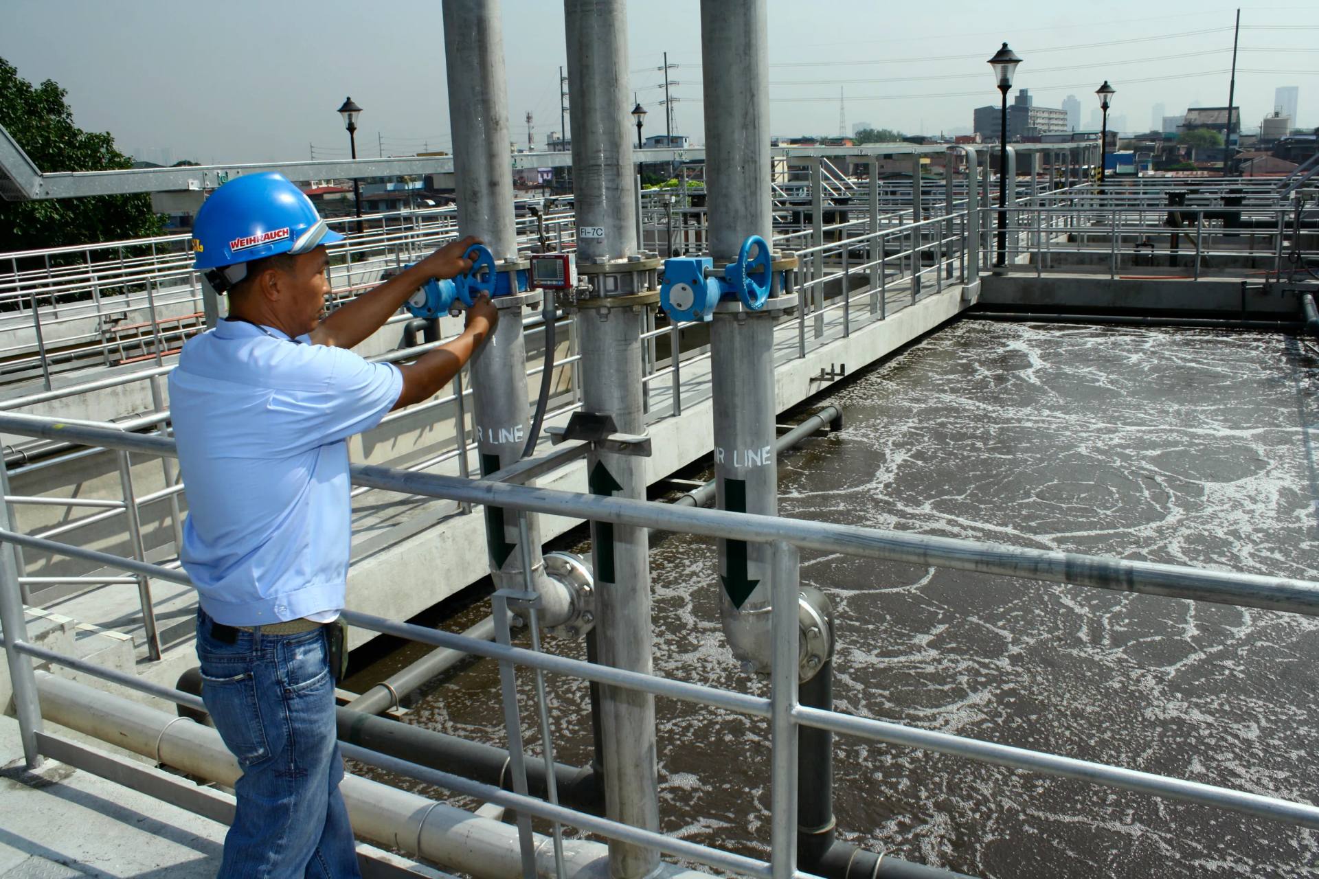 Aerial view of water treatment basins with a city skyline behind them.