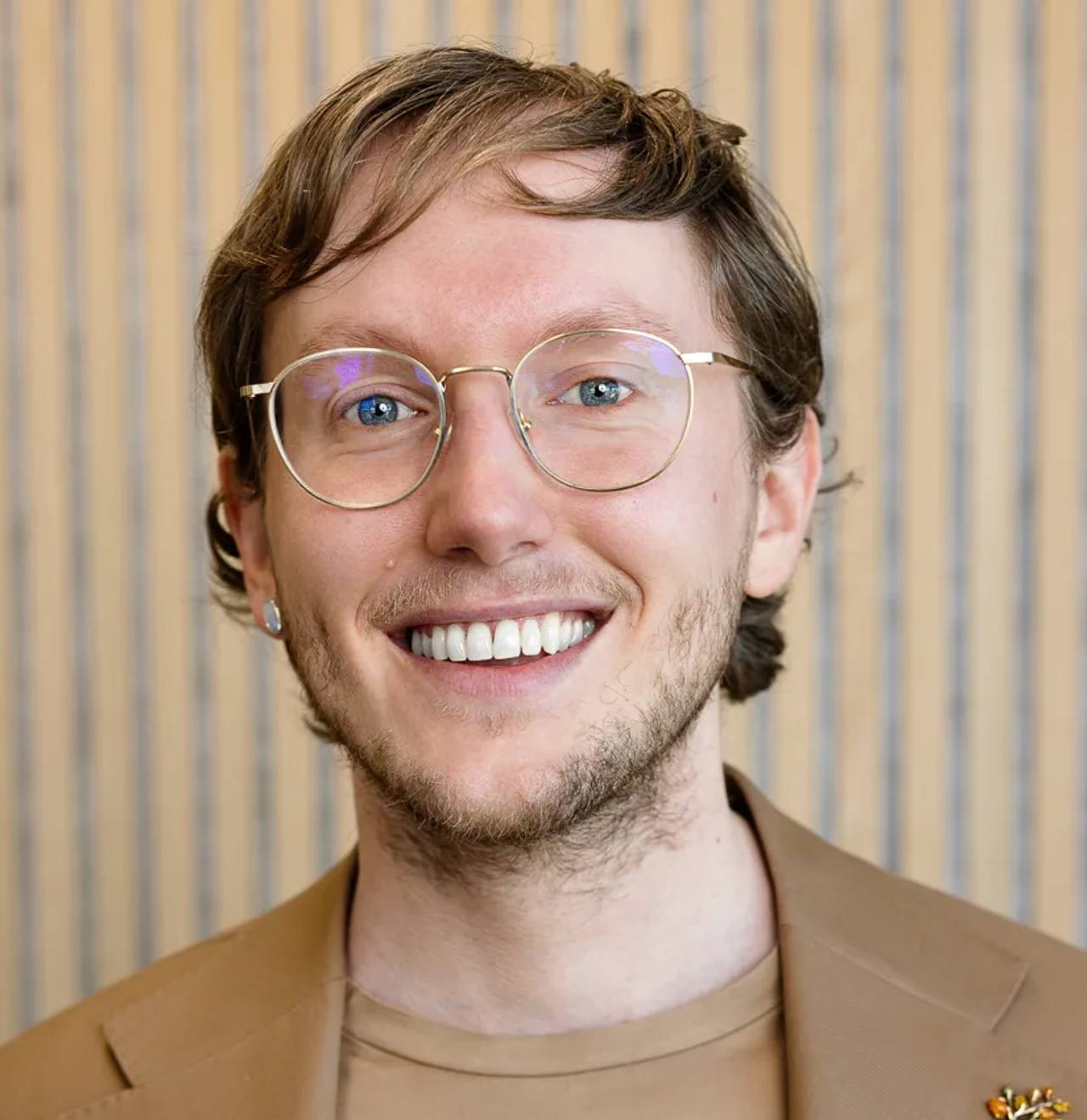 Portrait of Mr Sietse Blom in a beige jacket over a dark top, against a wooden slatted wall.