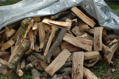 A pile of fire wood on the ground covered in a tarp