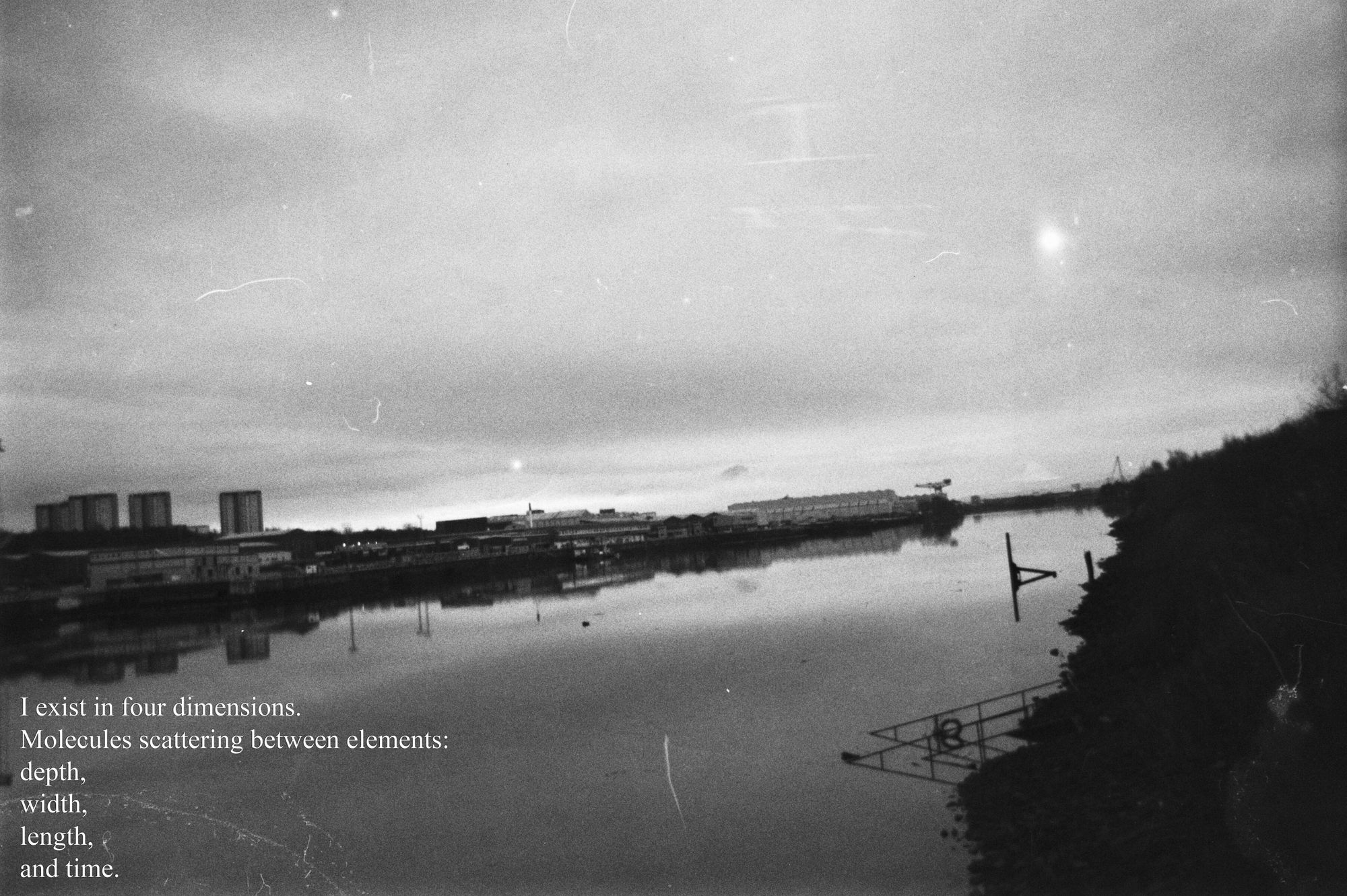Black and white photograph of a harbour. A river in the centre surrounded by buildings and dark shadows. White poetic text in the foreground.