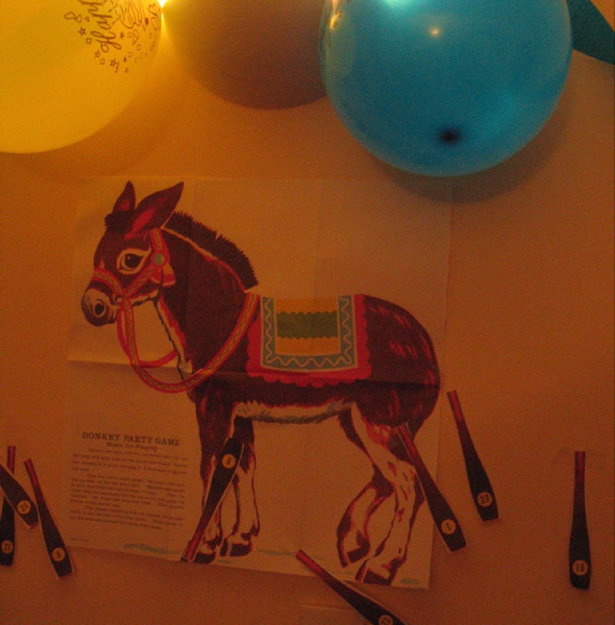 A picture of a pin-the-tail-on-the-donkey bathed in orange light. The donkey is surrounded by multi-coloured balloons.