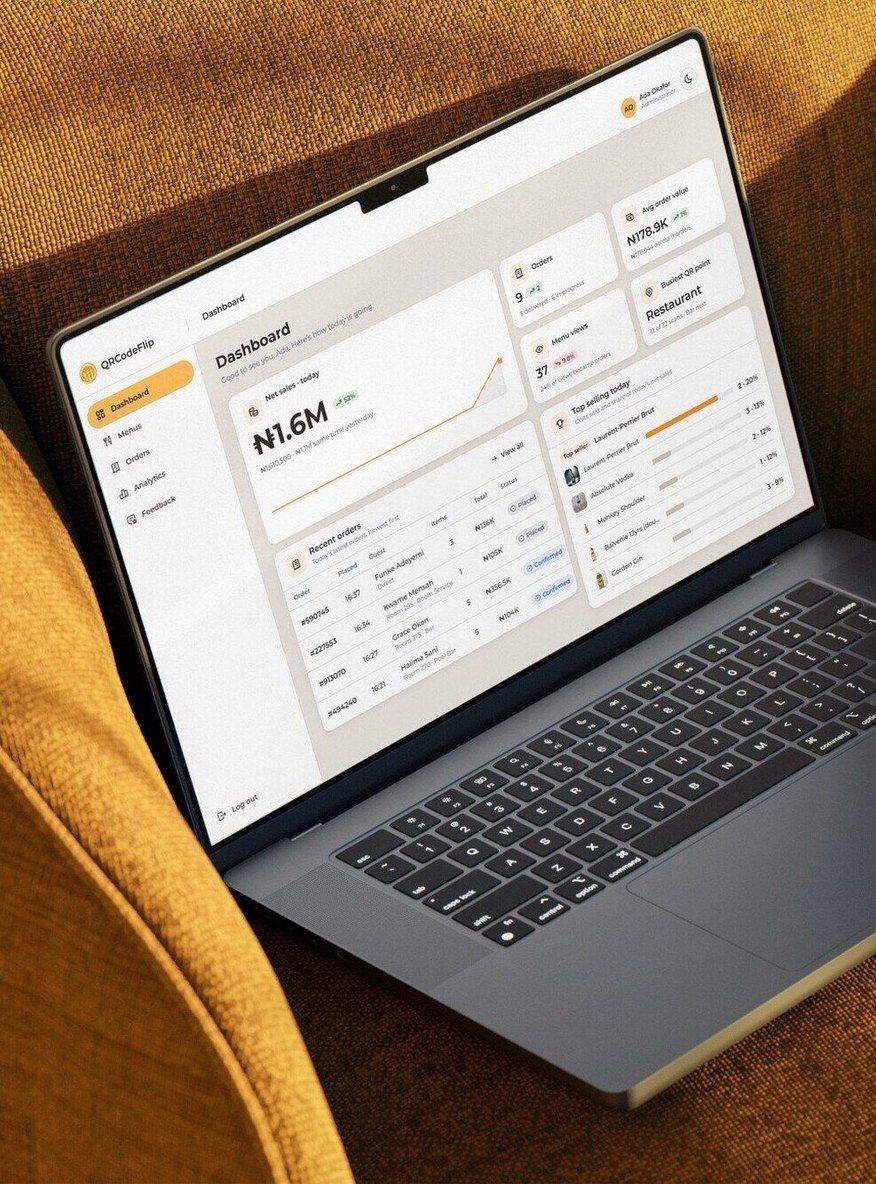 The QRCodeFlip admin dashboard on a laptop resting on a mustard armchair