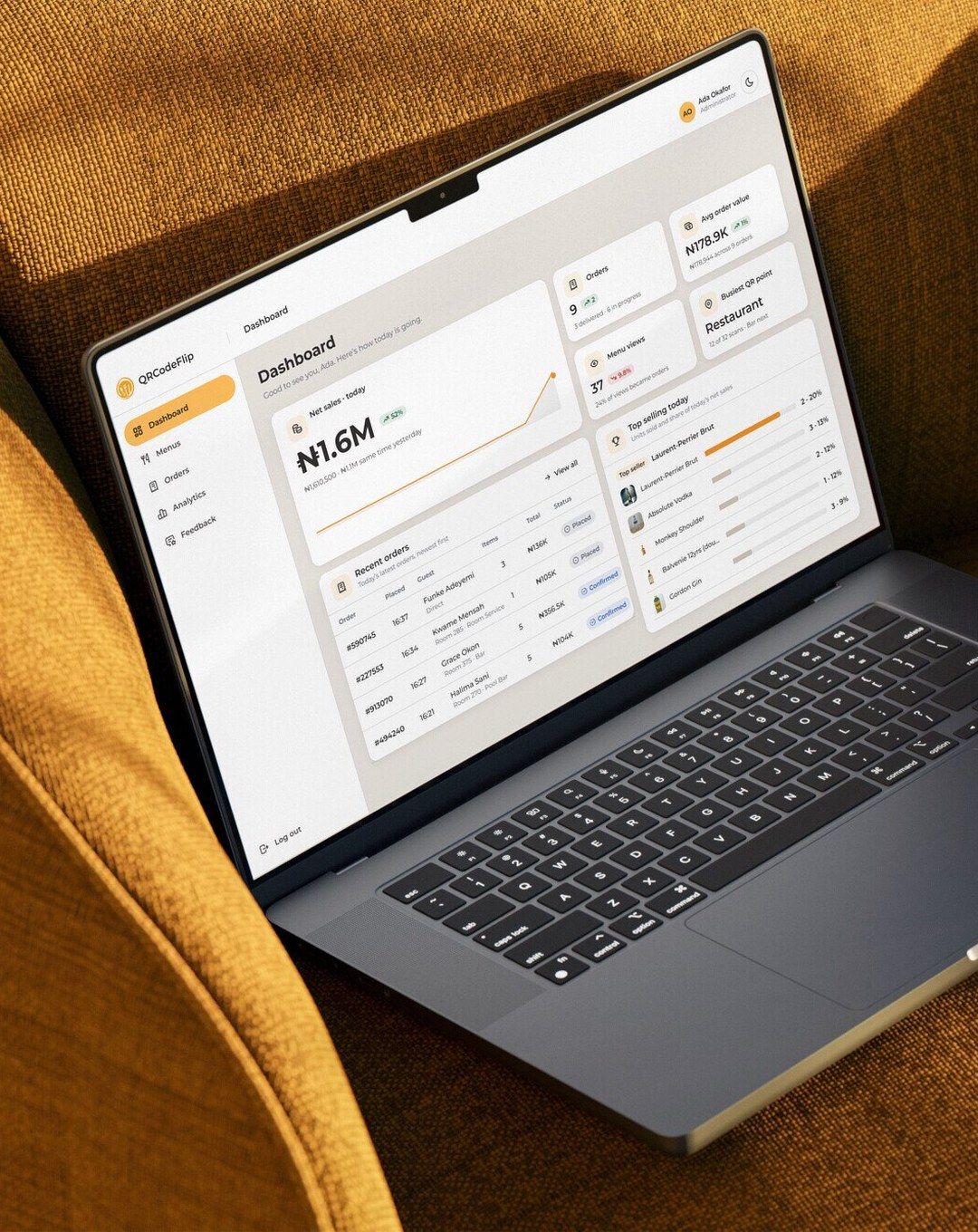 The QRCodeFlip admin dashboard on a laptop resting on a mustard armchair