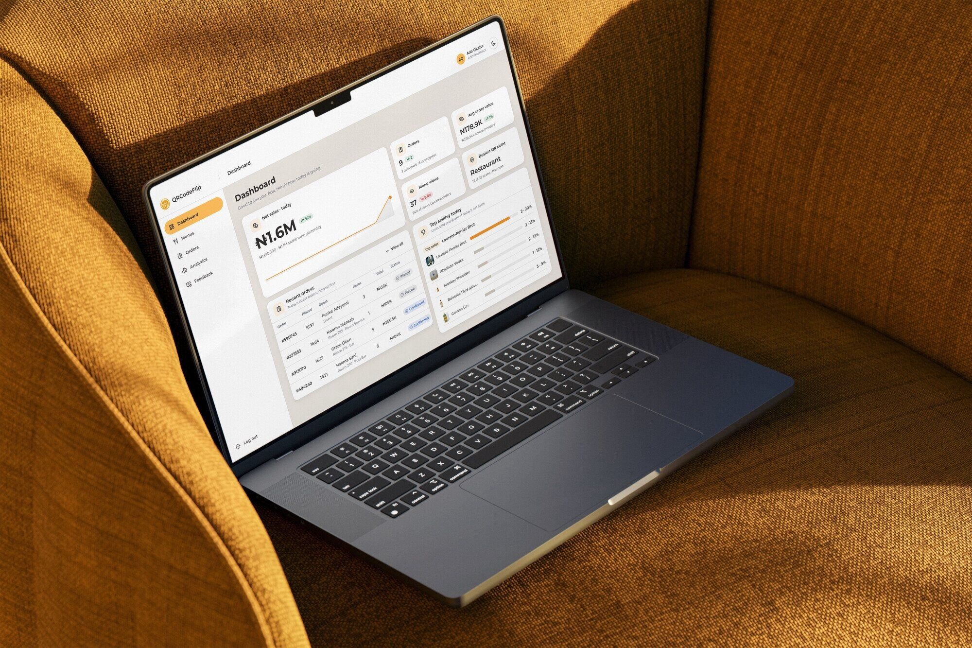The QRCodeFlip admin dashboard on a laptop resting on a mustard armchair: today’s net sales, orders, menu views, the busiest QR point, recent orders and top sellers