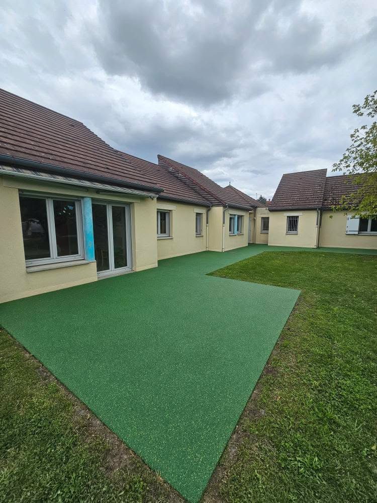 Cour de crèche avec sol amortissant vert, bleu et structure de jeu