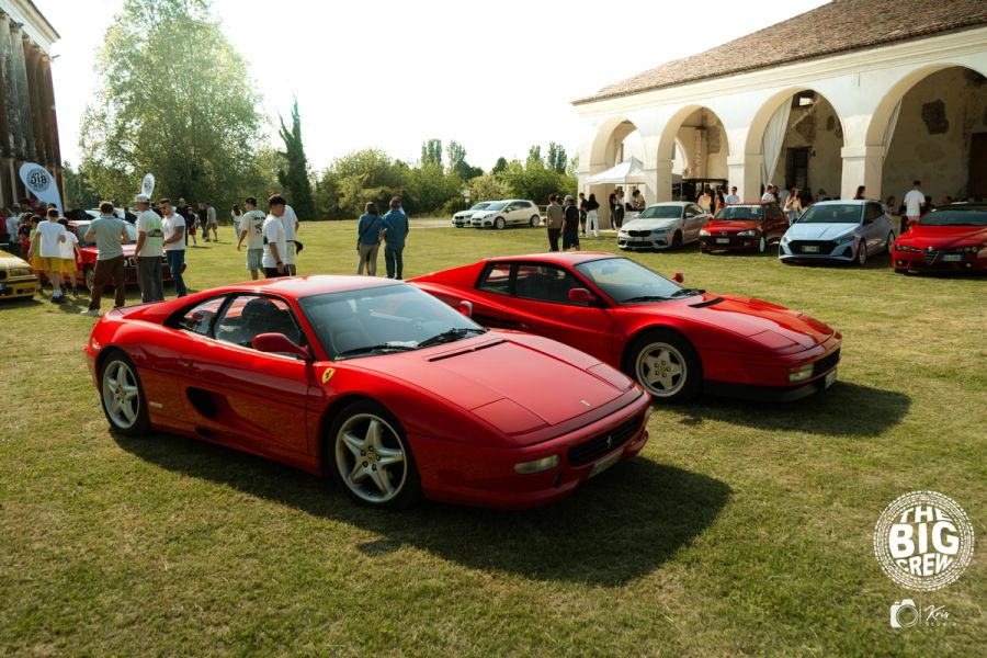 Due Ferrari rosse sul prato davanti a un edificio storico, con visitatori e altre auto sullo sfondo