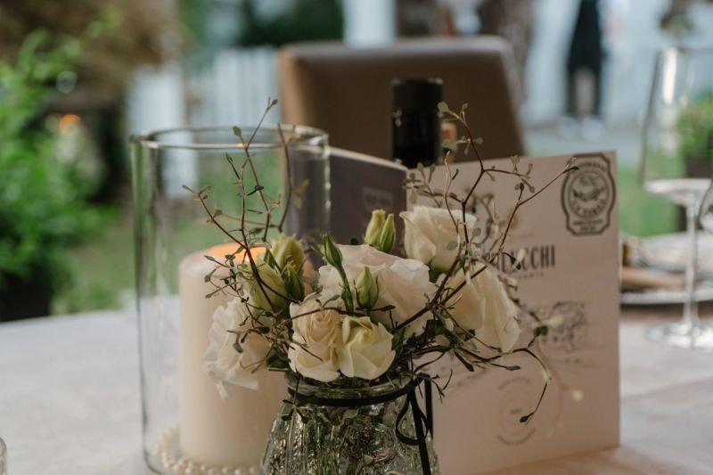 Rose bianche in un vasetto accanto a una candela e al menù, su un tavolo apparecchiato