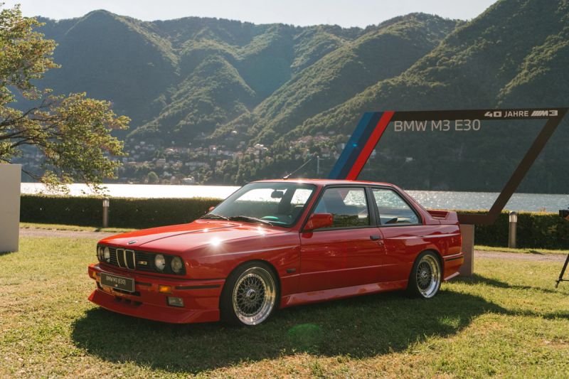 BMW M3 E30 rossa sul prato davanti al lago di Como, con la cornice «40 Jahre M3»