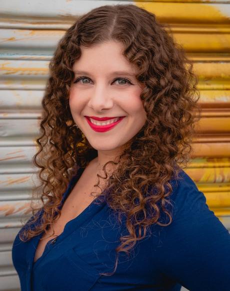 Romina Garber author photo with bright lipstick & an industrial background.