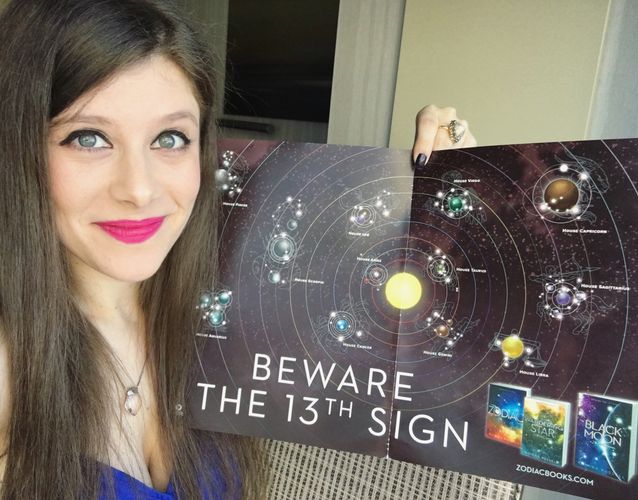 author Romina Russell holds up a printed constellation map of the Zodiac Galaxy
