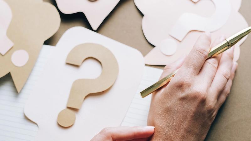 question marks on a paper. next to those papers are human hands with pen 