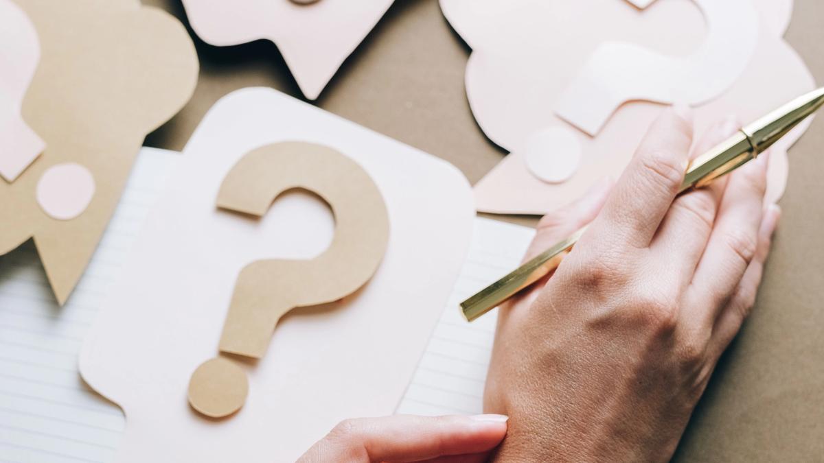 question marks on a paper. next to those papers are human hands with pen