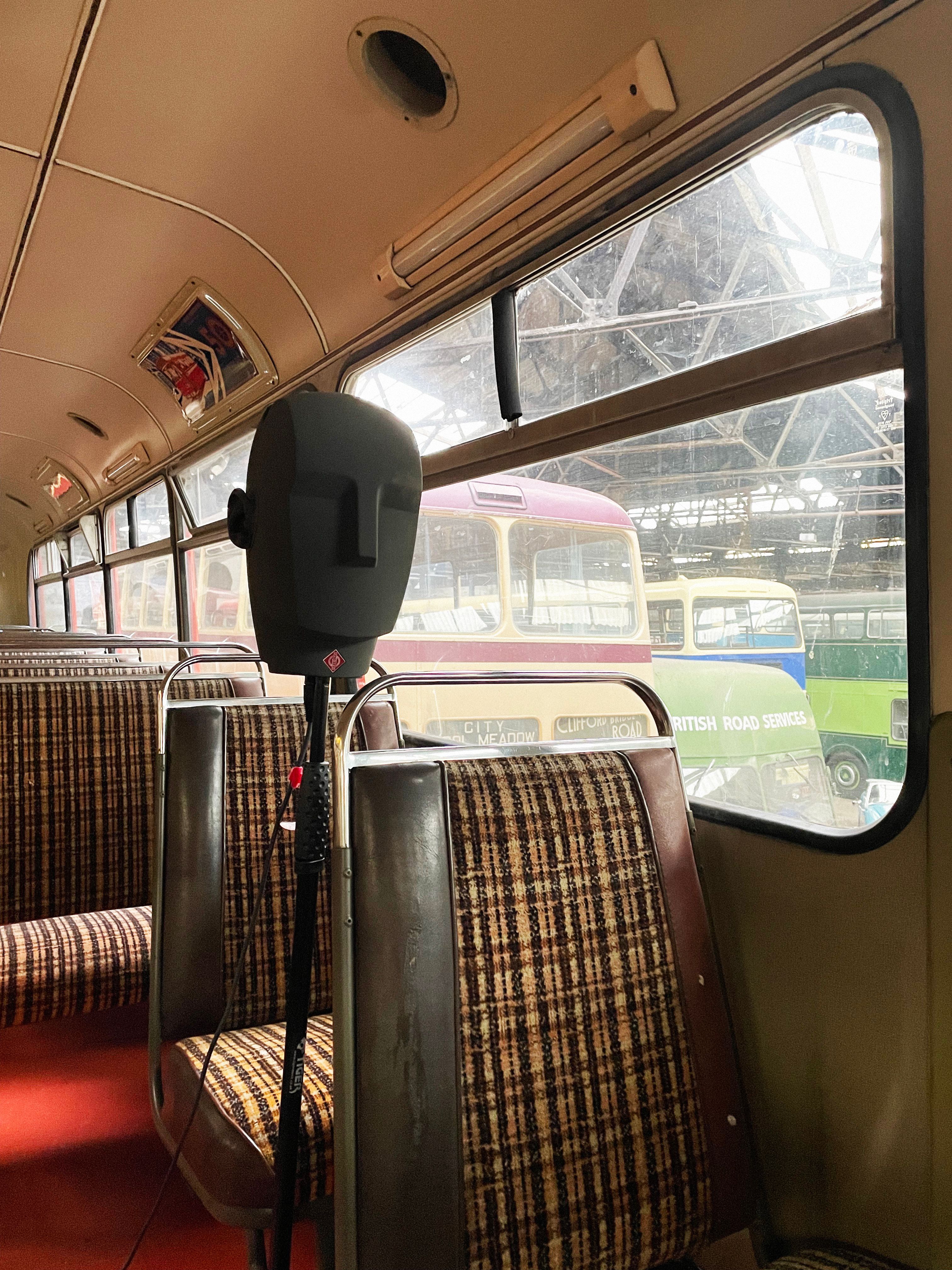 A grey binaural head on a microphone stand, with patterned bus seats
