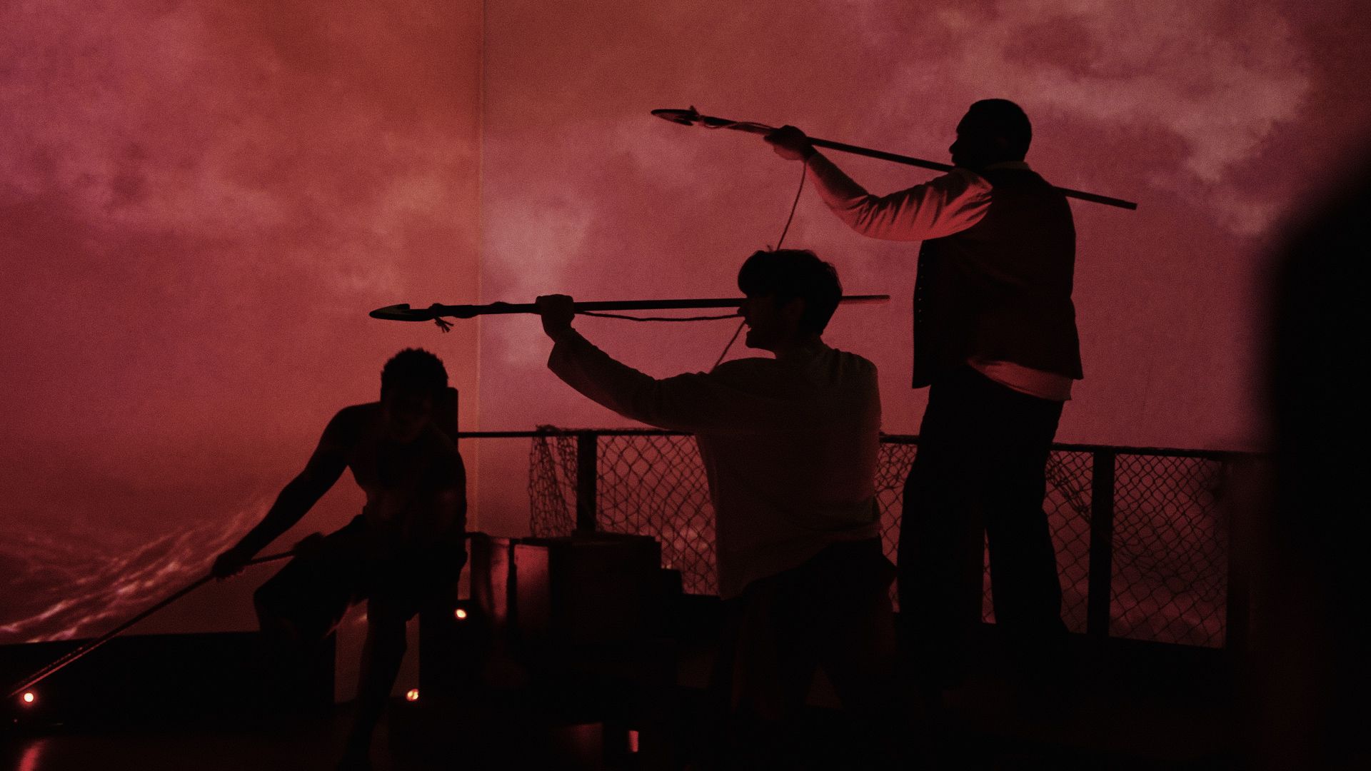 Three men with harpoons against red backdrop