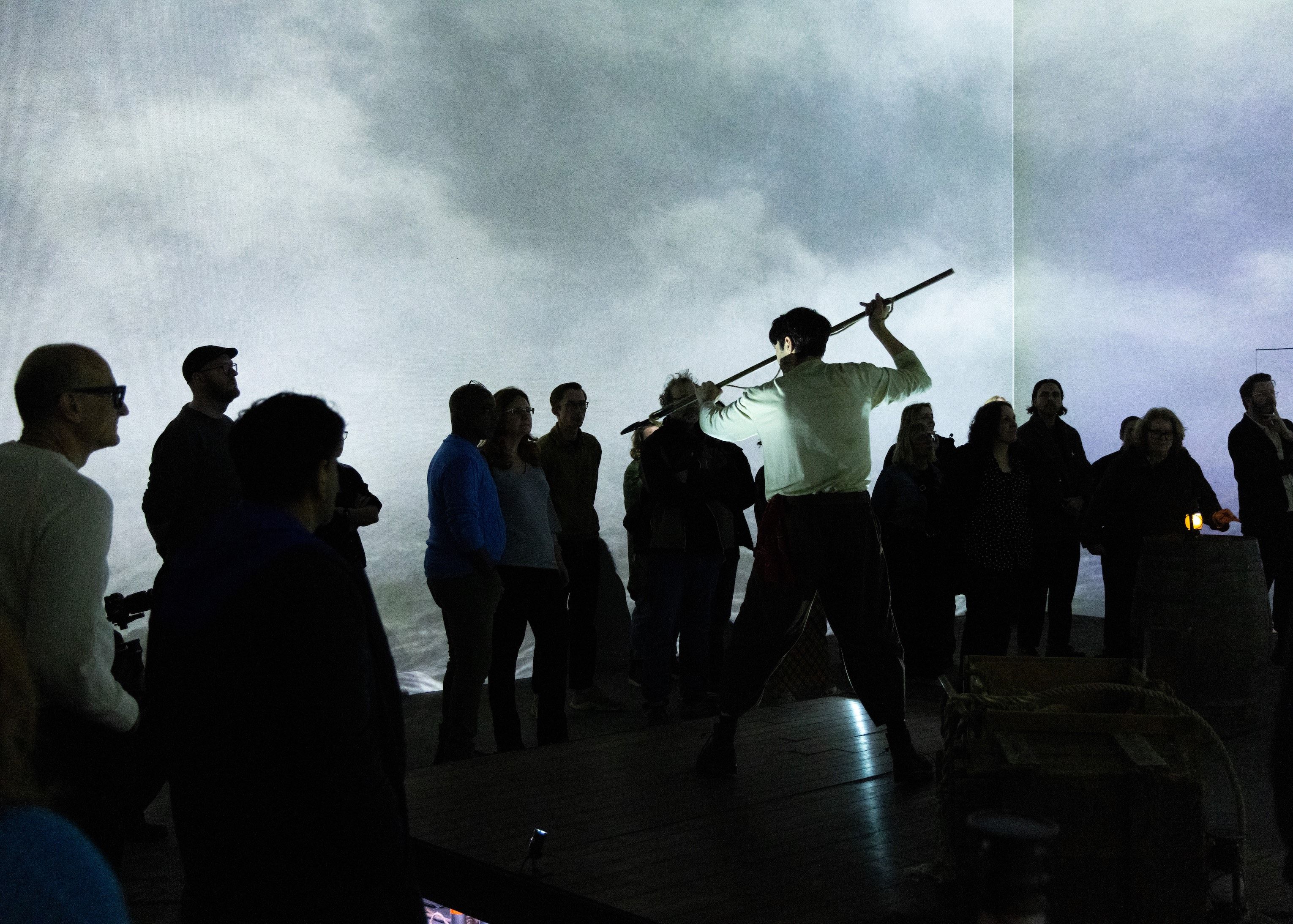 Man on stage with harpoon pointing at audience