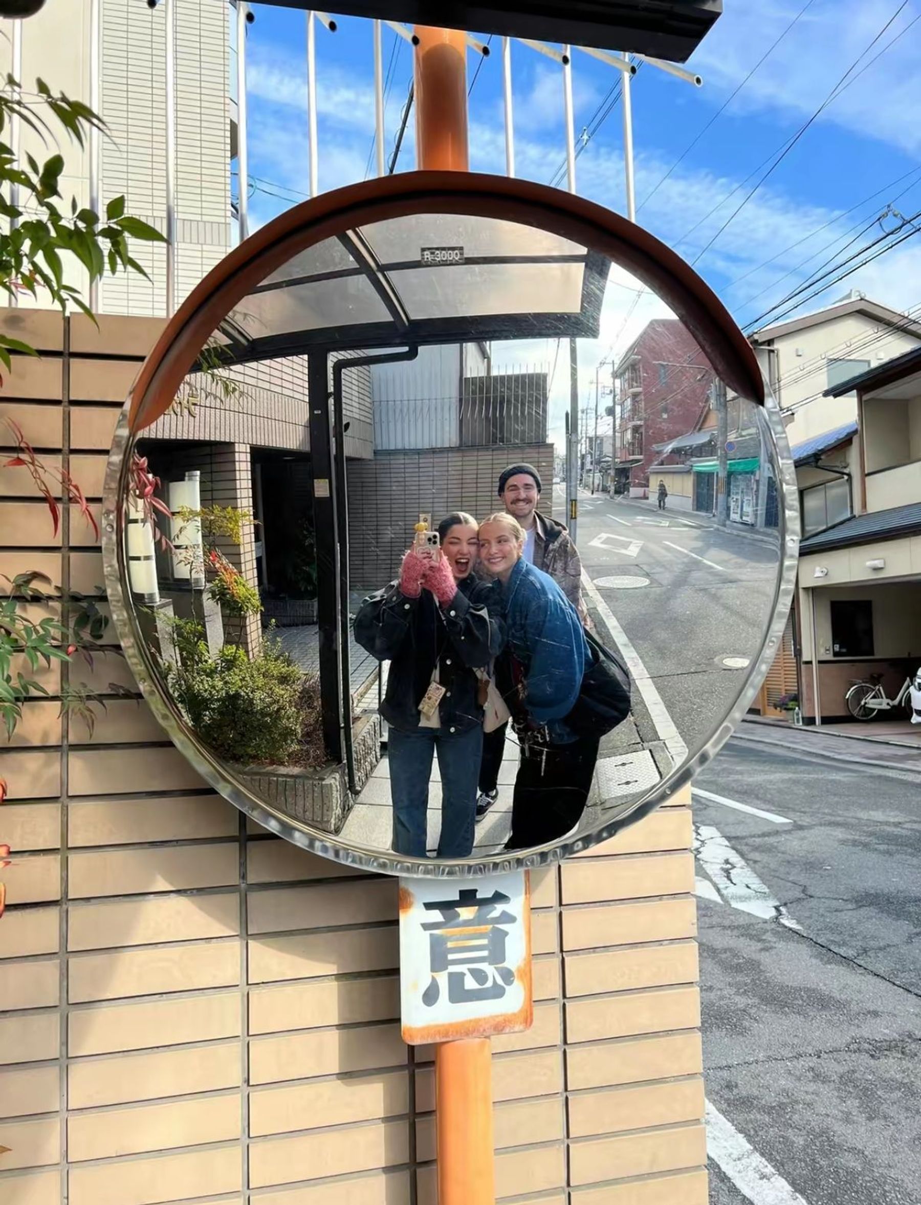 Three friends reflected in a convex street mirror in Tokyo.