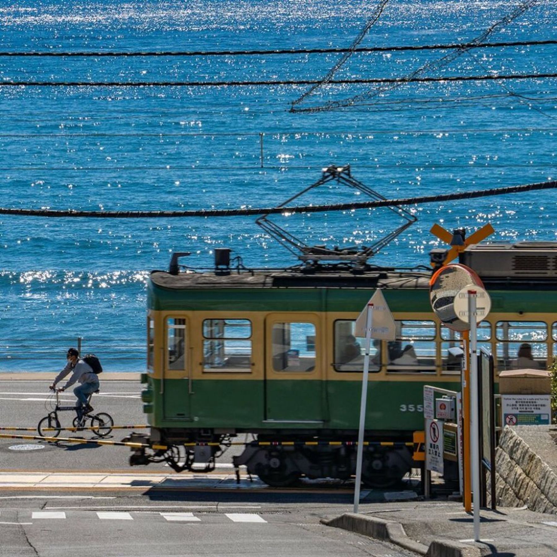 A green Enoden train passing beside the sea in Japan.