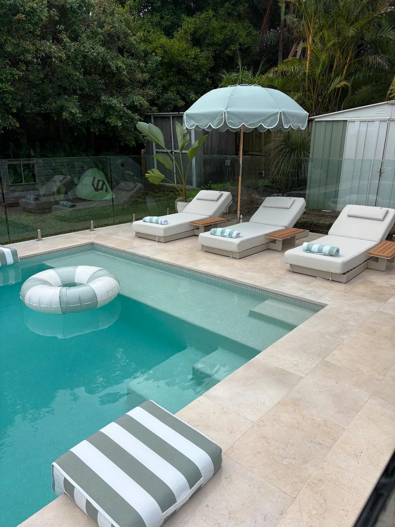 Travertine pool coping and paving with sun loungers under a green umbrella