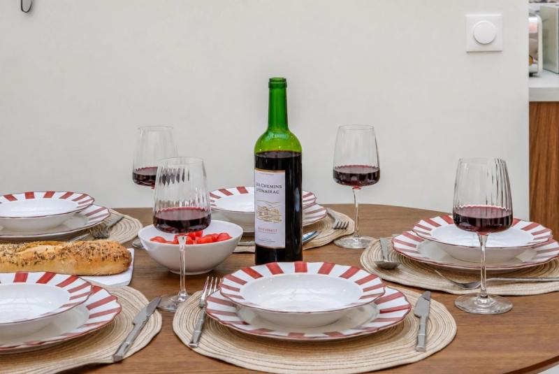 Wooden dining table set with red-striped plates, fluted wine glasses, and a bottle of Hérault red.
