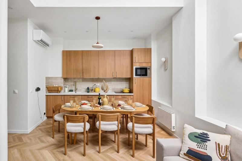 Open kitchen with oak cabinetry and a round dining table set for six on herringbone parquet.