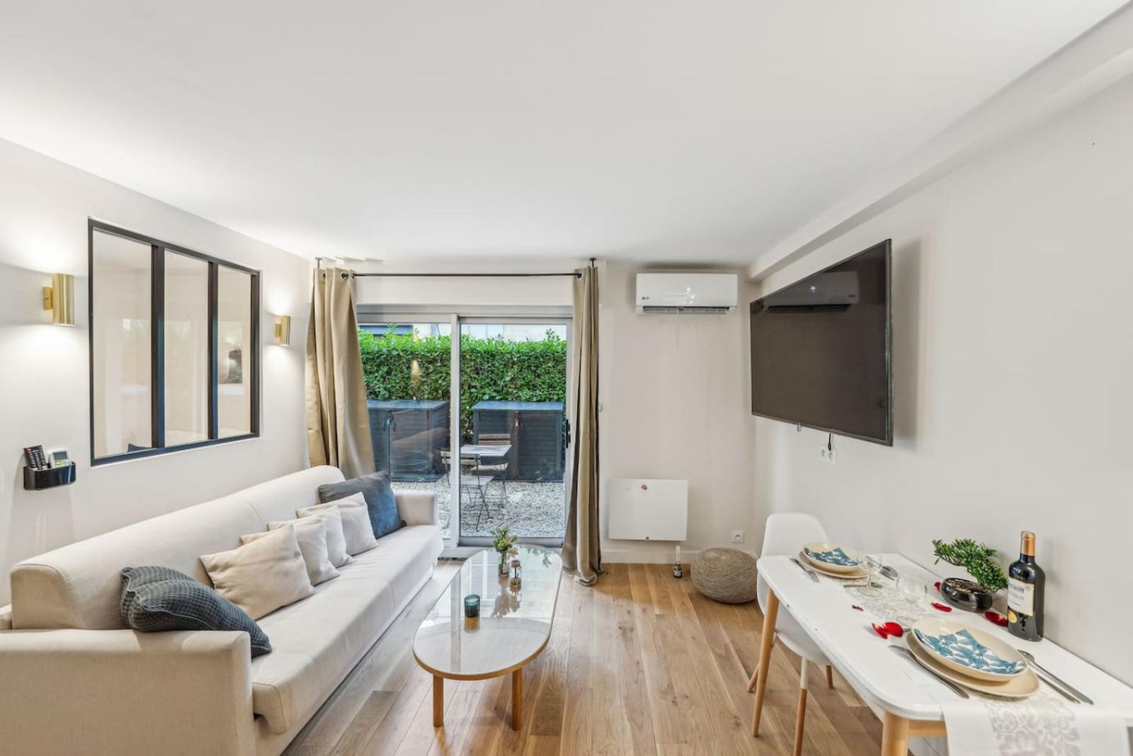 Living room with white sofa, interior steel-framed window, and sliding doors opening onto a hedged garden terrace.