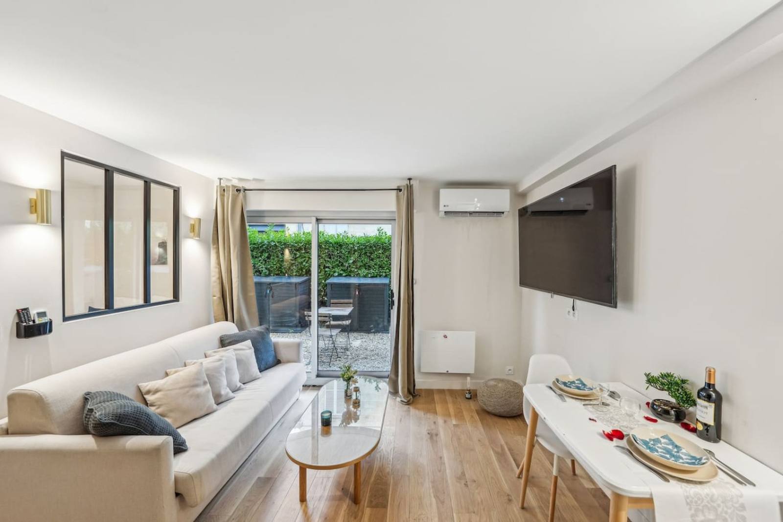 Living room with white sofa, interior steel-framed window, and sliding doors opening onto a hedged garden terrace.