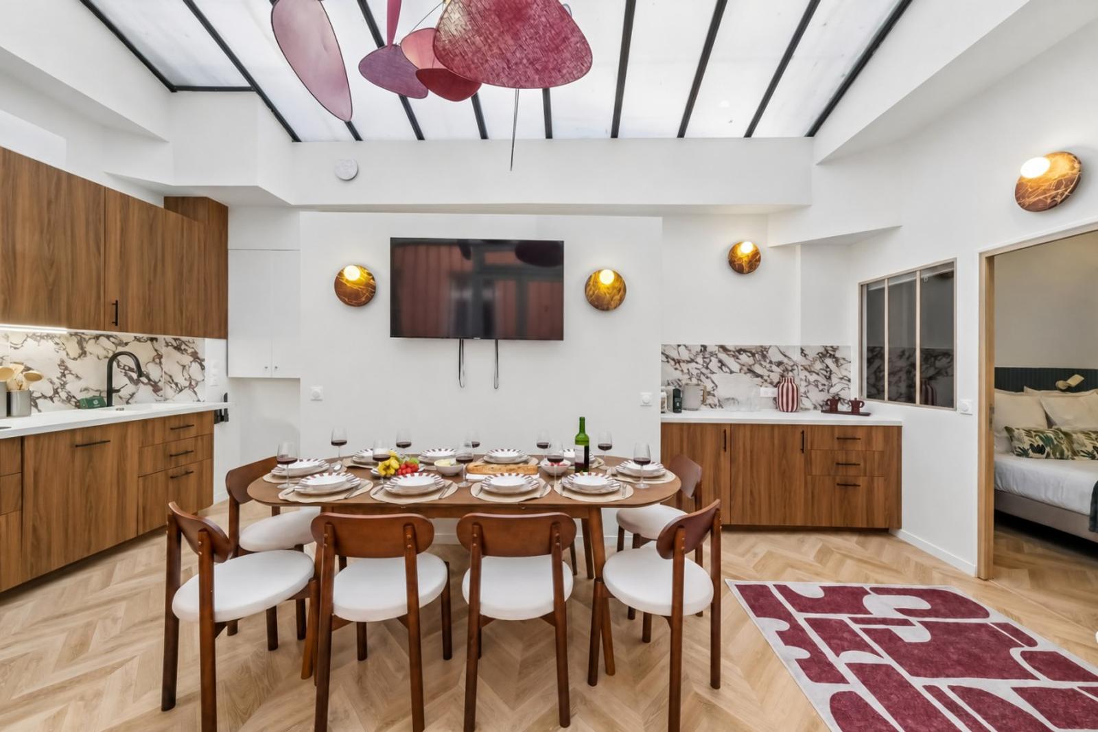 Dining room set for eight beneath a glass roof, with walnut cabinetry and marble backsplash framing the space.