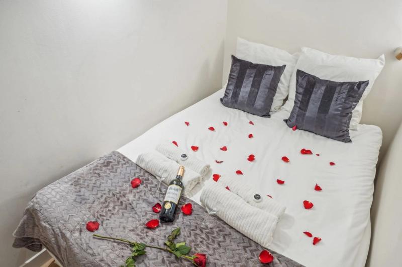 Double bed scattered with red rose petals, a wine bottle, and rolled white towels.